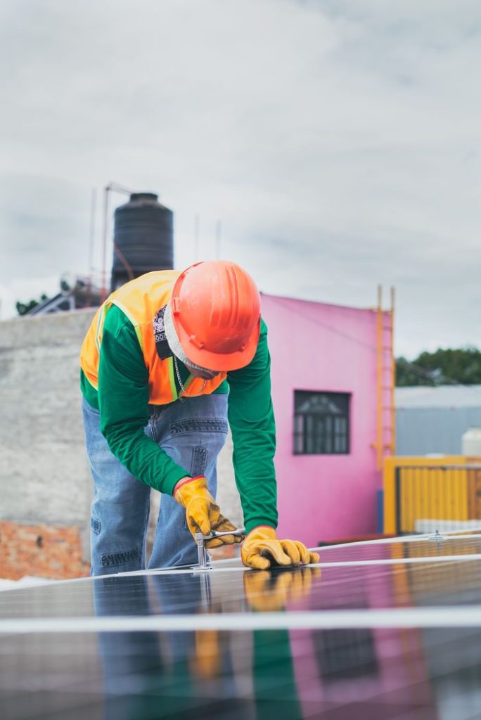 A solar technician working outdoors installing photovoltaic panels with safety gear.